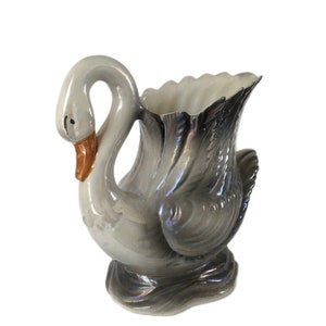 Könnte beinhalten: Eine weiße Keramik-Schwanen-Vase mit schillernden grauen und schwarzen Akzenten. Der Schwanenhals ist zu einem Griff gebogen, und die Vase hat eine breite Öffnung.
