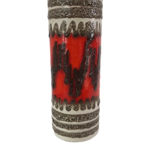 Könnte beinhalten: Eine zylindrische Keramikvase mit einer braunen und weißen texturierten Glasur. Die Vase hat ein rotes Band mit einem braunen abstrakten Design.