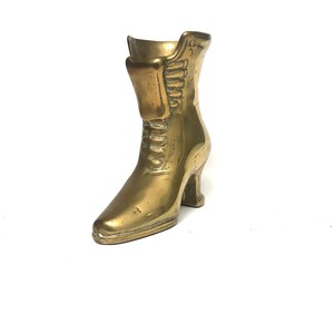 May include: A gold-colored metal boot figurine. The boot has a high heel and laces. The boot is a decorative object.