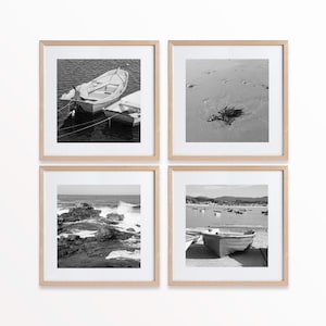 Può includere: Un set di quattro fotografie in bianco e nero incorniciate. Le immagini raffigurano scene costiere: barche sull'acqua, una spiaggia sabbiosa con alghe, onde che si infrangono sulle rocce e barche in un porto. Le cornici sono in legno chiaro.