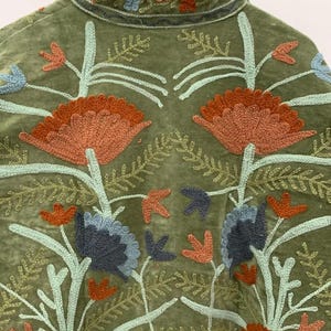 Pu&ograve; includere: Giacca verde oliva con ricami floreali intricati nei toni dell'arancione, blu e verde chiaro. La giacca presenta un colletto e cuciture dettagliate, mostrando un'estetica boh&eacute;mien.