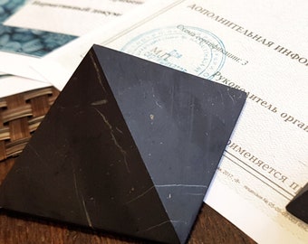 May include: A black pyramid-shaped object with a white marble-like pattern. The pyramid is sitting on a wooden surface.