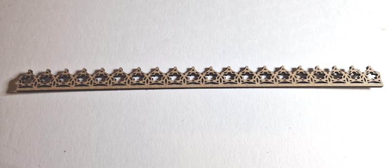 May include: A thin, wooden decorative trim piece with a repeating pattern of openwork star and triangle shapes. The trim is a light brown color and appears to be made of laser-cut wood. The design is symmetrical and suitable for craft projects.