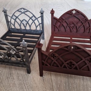 May include: Two miniature gothic-style beds. One is painted in a dark gray with silver accents, and the other is a deep burgundy. Both beds have ornate headboards and footboards with arched designs and decorative finials.