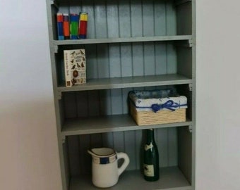 May include: A gray wooden bookshelf with five shelves. The shelves are filled with books, a wicker basket, a pitcher, a bottle, and a box. The bookshelf is about 3 feet tall.