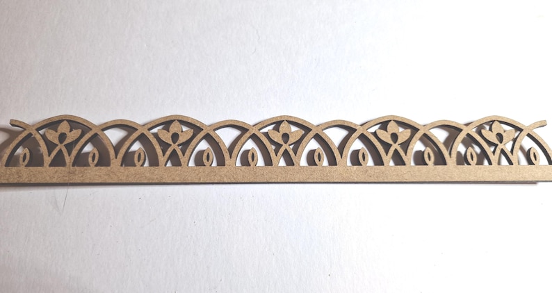 May include: A decorative wooden trim piece with a repeating floral and arched design. The trim is a light brown color and features cut-out details of flowers and oval shapes. The design is symmetrical and suitable for craft projects.