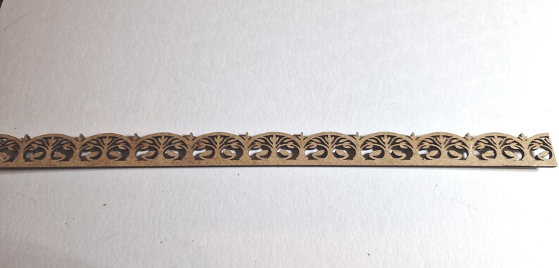 May include: A decorative wooden trim piece with a repeating tree and arch design. The trim is a light brown color and has a series of arched cutouts. The design is symmetrical and suitable for craft projects or home decor.