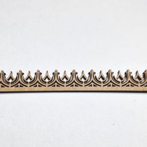 May include: A laser-cut wooden decorative trim piece with a repeating crown design. The trim is a light brown color and features intricate cut-out patterns. The piece is ideal for craft projects and home decor.