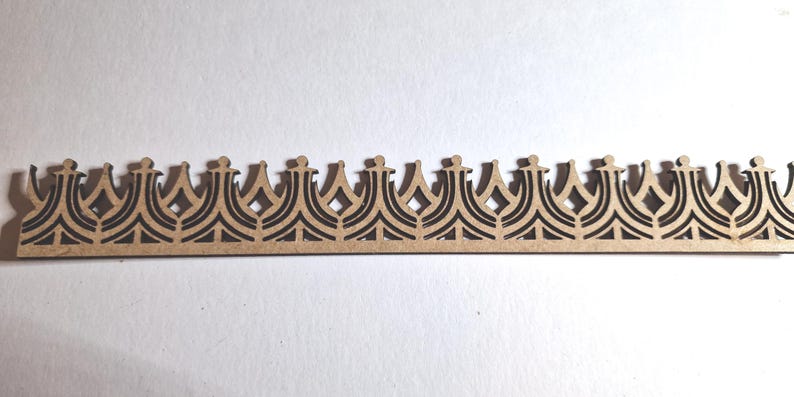 May include: A decorative wooden crown-shaped border with a repeating pattern. The border is made of light brown wood with a dark brown, intricate design. The design features a series of crown shapes with diamond and arch details. This item is suitable for craft projects.