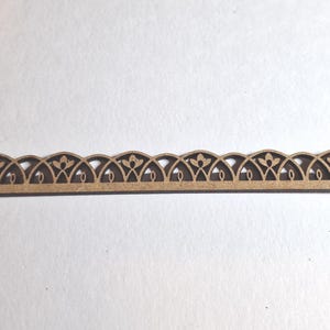 May include: A decorative wooden trim piece with an intricate, repeating arched design. The trim is a light brown color and features cut-out floral and curved patterns. The piece is long and narrow, suitable for craft projects or home decor.