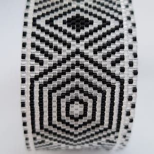 May include: A black and white beaded bracelet with a geometric pattern. The bracelet is made of small, square beads that are arranged in a repeating pattern.