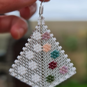 May include: A pair of white beaded earrings with a geometric design. The earrings feature small colorful beads in shades of pink, green, and red.