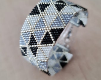 Peut inclure: Un bracelet en perles avec un motif géométrique en noir, blanc et gris.