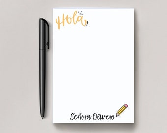Puede incluir: Un bloc de notas blanco con la palabra "Hola" escrita en amarillo en la parte superior. La parte inferior del bloc de notas tiene el texto "Señora Olivero" y un pequeño dibujo de lápiz amarillo.