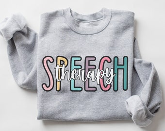 May include: A gray sweatshirt with the words "SPEECH therapy" printed on the front in colorful letters. The letters are outlined in black and have a white interior.