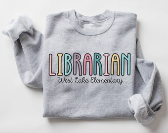 May include: Gray sweatshirt with the text "LIBRARIAN" in rainbow colors and "West Lake Elementary" in black text below.