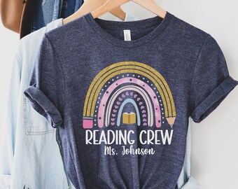 May include: A navy blue t-shirt with a rainbow design and the text "Reading Crew Ms. Johnson".