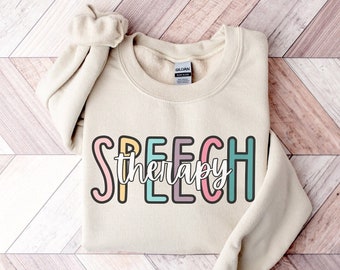 May include: A beige sweatshirt with the text "SPEECH therapy" in colorful letters. The letters are outlined in black and have a whimsical, hand-drawn style.