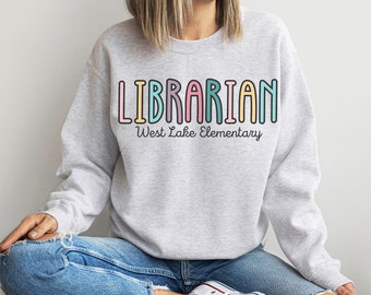 May include: Gray sweatshirt with the text "LIBRARIAN" in rainbow colors and "West Lake Elementary" in black text below.