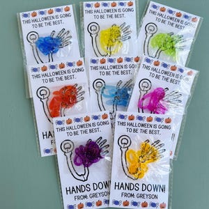May include: Eight small bags with colorful plastic skeleton hands and the text "This Halloween is going to be the best."  The bags are labeled "Hands Down!" with the name "Greyson".