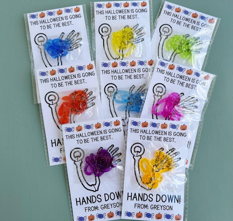 May include: Eight small bags with colorful plastic skeleton hands and the text "This Halloween is going to be the best."  The bags are labeled "Hands Down!" with the name "Greyson".