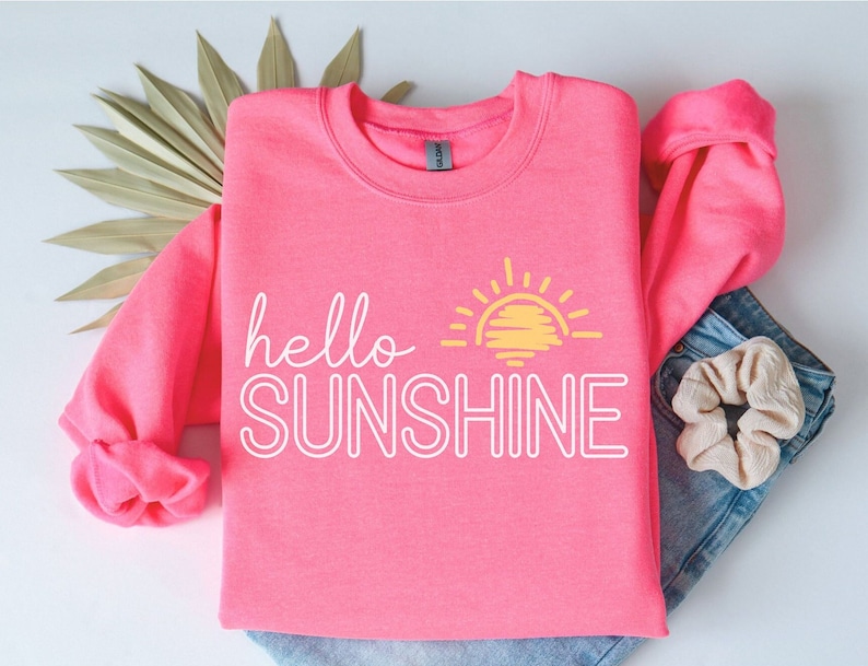 May include: A pink sweatshirt with the text "hello sunshine" in white outlined letters and a yellow sun graphic.