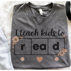 May include: Gray t-shirt with the text "I teach kids to read" in black lettering. The word "read" is broken up into three squares with a flower design on either side.