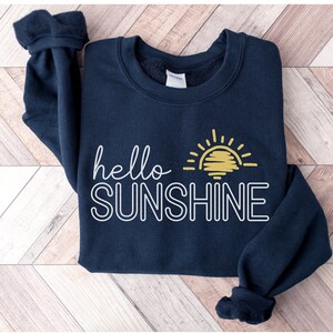 May include: A navy blue sweatshirt with a white outline of the text "hello sunshine" and a yellow sun graphic.