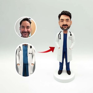 Könnte beinhalten: Figur einer Arztfigur in weißem Laborkittel, blauer Kleidung und schwarzen Schuhen. Der Arzt hat ein Stethoskop und ein Namensschild mit der Aufschrift "Jared Smith, M.D.". Die Figur steht auf einem weißen Sockel. Ca. 15 cm hoch.