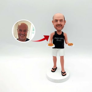 Könnte beinhalten: Eine personalisierte Wackelkopf-Figur eines Mannes in einem schwarzen Tanktop und weißen Shorts, der zwei Teller Spaghetti hält. Die Figur trägt schwarze Flip-Flops und steht auf einem weißen Sockel. Ein Foto des Mannes befindet sich in einem Kreis.