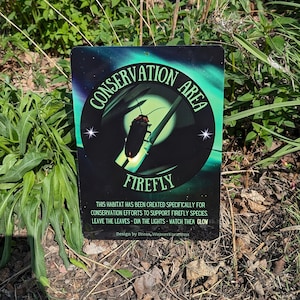 May include: A black and green sign with a white circle that says "Conservation Area Firefly" with a stylized image of a firefly inside the circle. The sign also includes the text "This habitat has been created specifically for conservation efforts to support firefly species. Leave the leaves - dim the lights - watch them glow. Design by Dream, WeaverKreations."