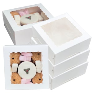 Puede incluir: Cajas de cartón blanco con ventanas de plástico transparente, cada una contiene una variedad de pequeños dulces coloridos. Los dulces incluyen galletas, caramelos y un pequeño pastel con un diseño de acebo.