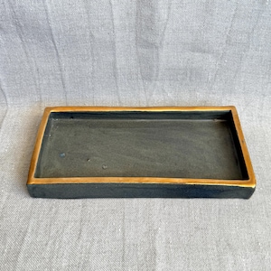 Può includere: Un vassoio rettangolare in ceramica nera con un bordo dorato. Il vassoio è perfetto per servire spuntini o per contenere piccoli oggetti.