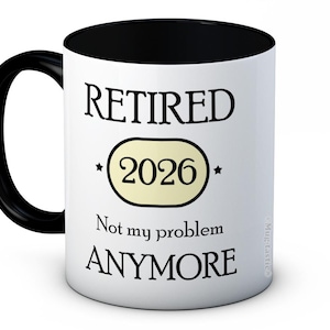 Puede incluir: Taza de cerámica blanca con asa e interior negros. La taza presenta el texto "RETIRED 2026 Not my problem ANYMORE" en negro, con el año 2026 dentro de un óvalo amarillo claro.