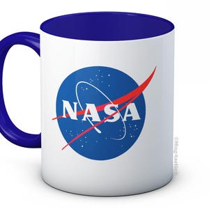May include: White ceramic mug with a blue interior and handle. The mug features the NASA logo in a blue circle with a red swoosh and the word "NASA" in white. The mug is a standard size for coffee or tea.