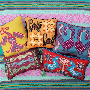 May include: Five colorful embroidered throw pillows with various designs, including birds, cats, and geometric patterns. The pillows are arranged on a striped turquoise and pink fabric.