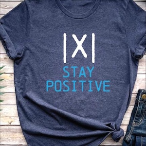 May include: A dark blue t-shirt with white text that says "|X| STAY POSITIVE" in a handwritten style.