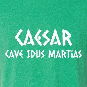 May include: Green t-shirt with white text that reads "CAESAR CAVE IDUS MARTIAS".