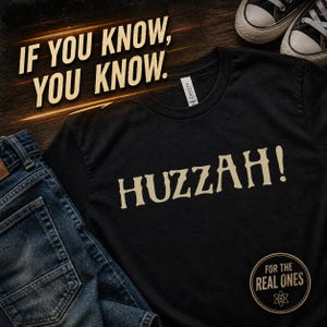 May include: Black t-shirt with the word "Huzzah!" in a serif font. The phrase "If you know, you know" is above the shirt. Blue jeans and black sneakers are also in the image. The phrase "For the real ones" is in a circle at the bottom.
