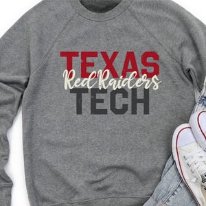 May include: A heather gray sweatshirt with the words "TEXAS Red Raiders TECH" in red, white, and black lettering. White canvas sneakers and denim jeans are visible in the image.