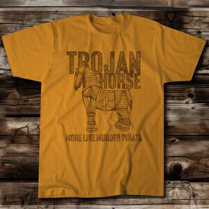 Image of the Trojan Horse (Dark Brown Ink) with the words Trojan Horse….More like Murder Pinata.  On a Next Level Antique Gold shirt