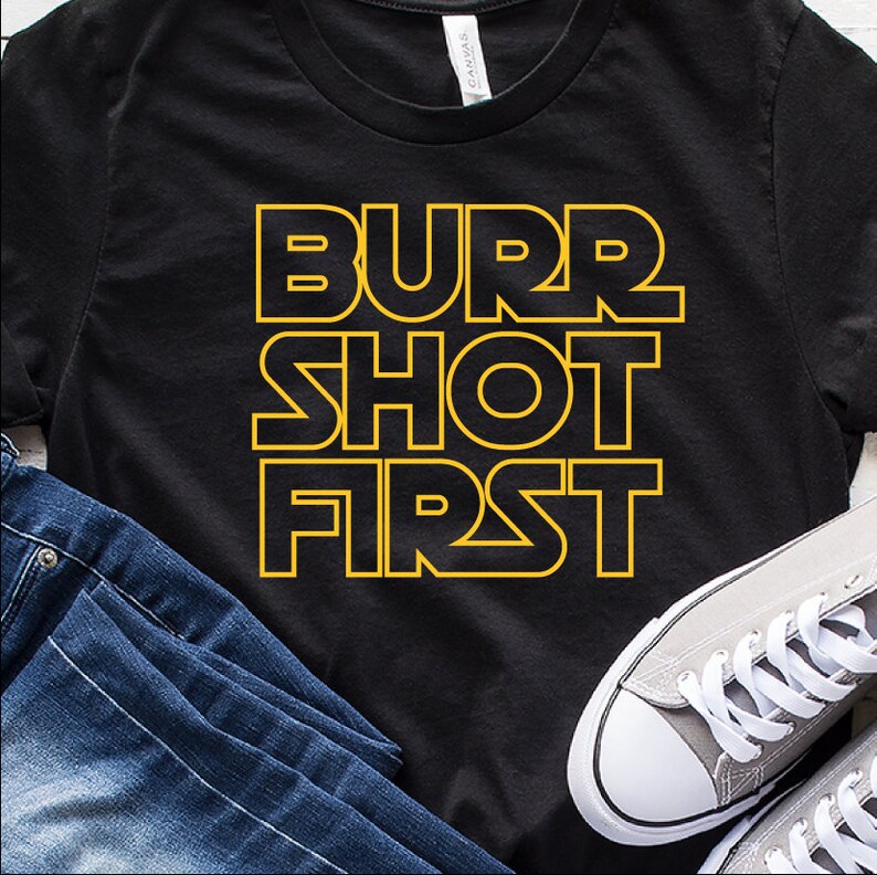 Pode incluir: Camiseta preta com o texto "Burr Shot First" em letras amarelas com contorno.