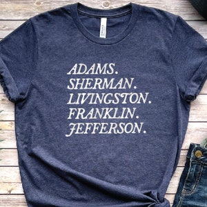 May include: A navy blue t-shirt with white text that reads "ADAMS. SHERMAN. LIVINGSTON. FRANKLIN. JEFFERSON."