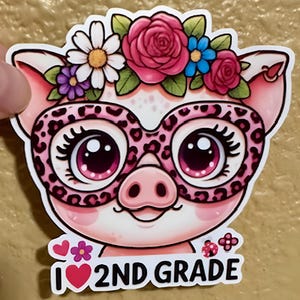 May include: A sticker featuring a cartoon pig with pink skin, wearing leopard print glasses and a floral crown. The pig has large, expressive eyes and the text "I ❤️ 2ND GRADE" at the bottom. The sticker is held by a hand.