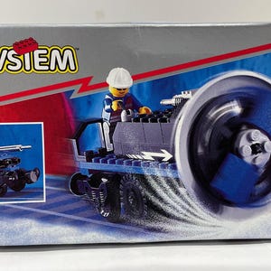 May include: A LEGO System box featuring a blue and black vehicle with a minifigure. The box has the LEGO logo and the number 4533. The box also shows a smaller image of the vehicle. The recommended age is 7-12.