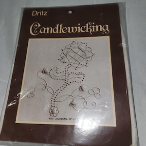 May include: A Dritz Candlewicking kit in a sealed plastic package. The kit features a floral design with the text "Candlewicking" in a decorative font. The design is on a beige background, and the package is brown. The dimensions are 12" x 17".