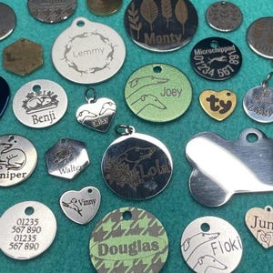 May include: A selection of pet tags in various shapes and sizes. The metal tags feature engraved names, dog illustrations, and contact details. Some tags have decorative patterns and designs, suitable for pets.
