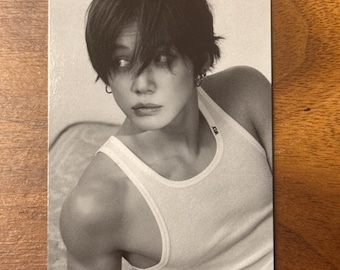May include: A rectangular black and white photo card featuring a person with short dark hair wearing a white ribbed vest top with the text WLY printed on the shoulder strap. The person is looking to the side with a neutral expression.