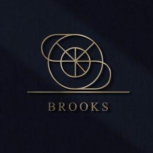 Può includere: Un design di logo dorato con un motivo circolare geometrico e la parola "BROOKS" in un font sans-serif.