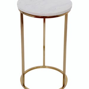 May include: A round side table with a white marble top and a gold-coloured metal frame. The table has a circular base and three straight legs. The table is approximately 51 cm tall.
